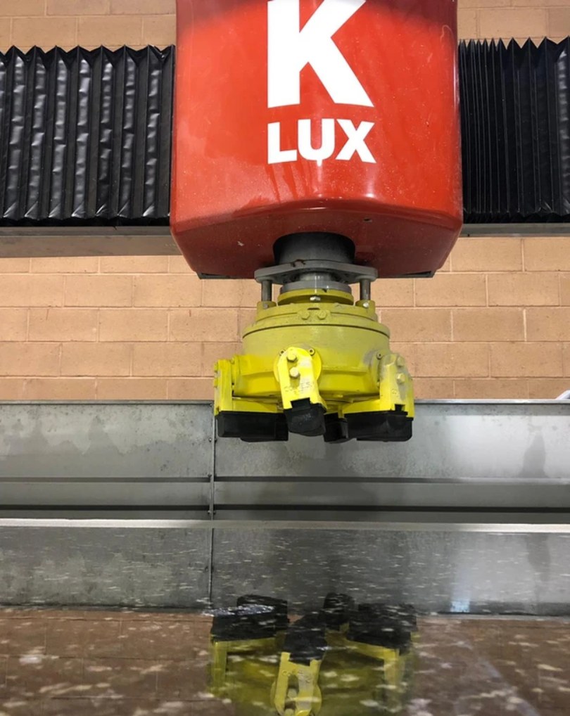 The finishing head lowered over the machine bed, reflected in the water below it